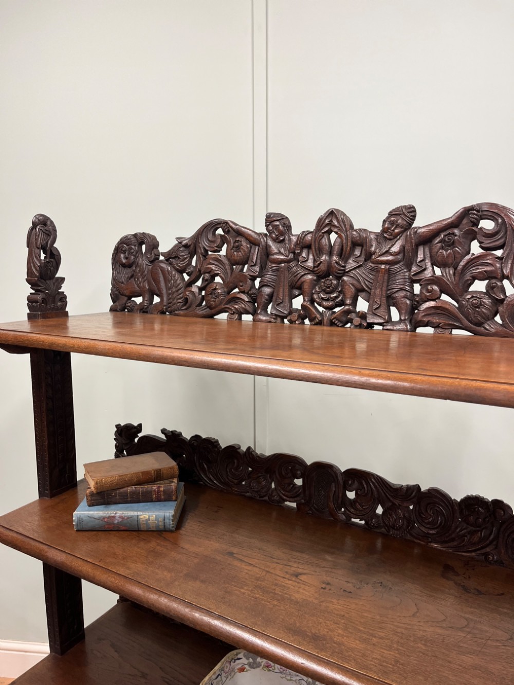 A 19th-century carved dark teak three-tier buffet featuring relief-carved backboard galleries with figurative motifs, supported on carved uprights and trestle feet. View VI