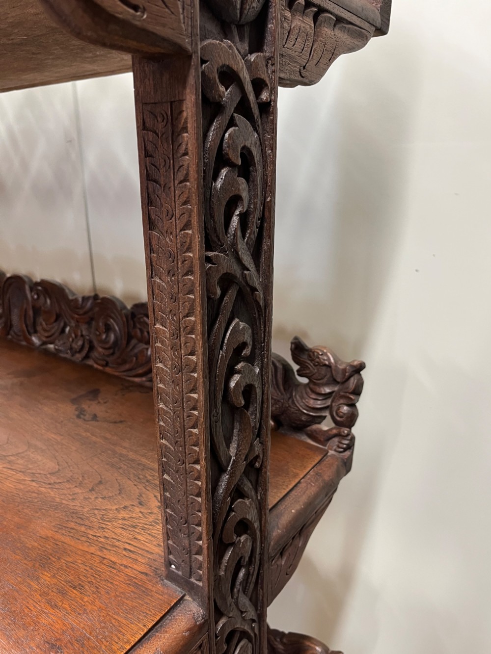 A 19th-century carved dark teak three-tier buffet featuring relief-carved backboard galleries with figurative motifs, supported on carved uprights and trestle feet. View X