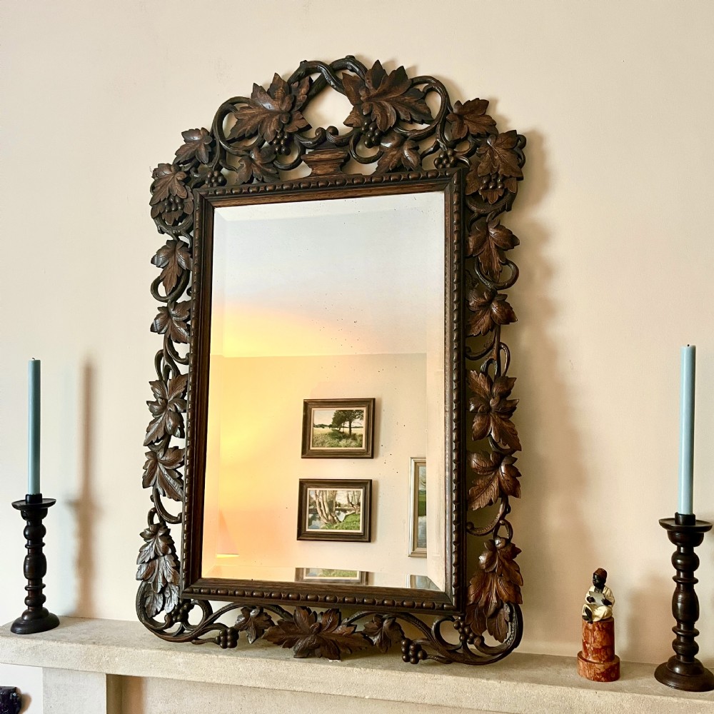 A rectangular nineteenth-century mirror with a heavily hand-carved dark oak frame featuring carved vine leaves, grapes, and foliage.