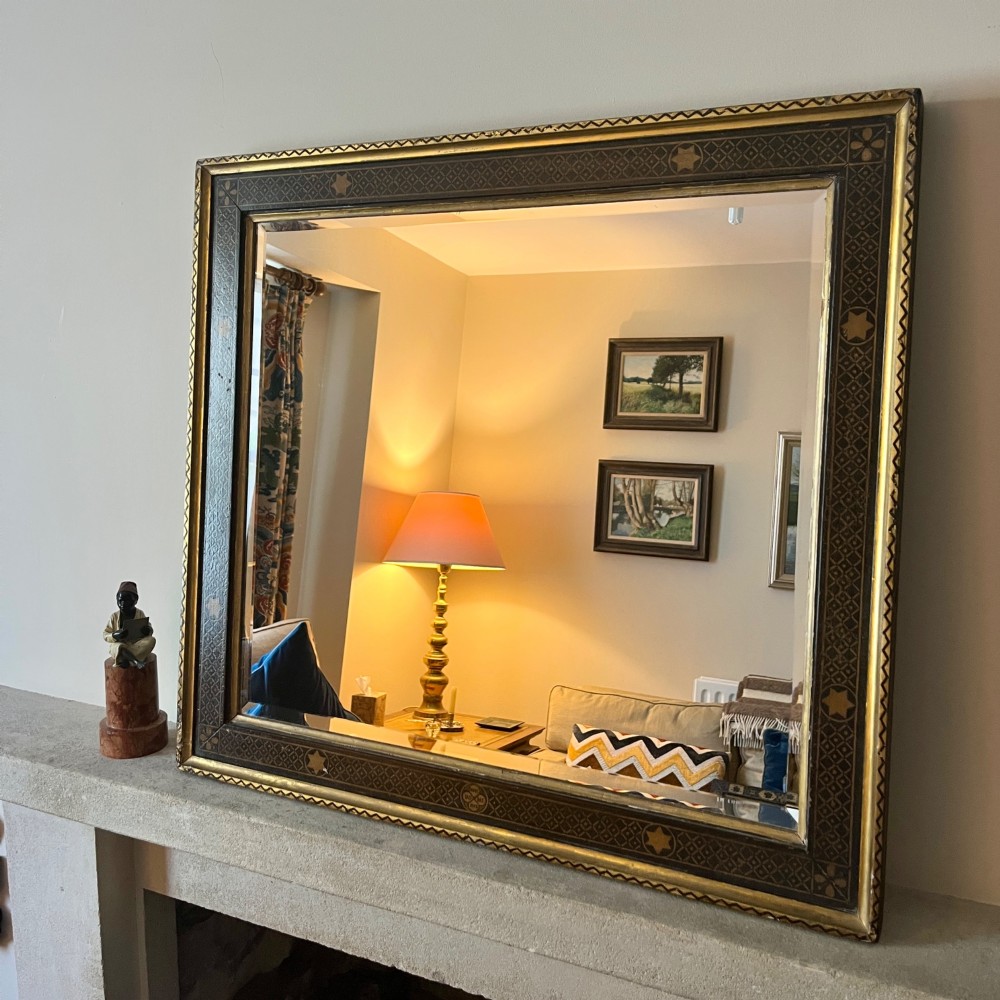 A large nineteenth-century rectangular wall mirror featuring a dark painted frame embellished with geometric motifs and a gilded outer border.