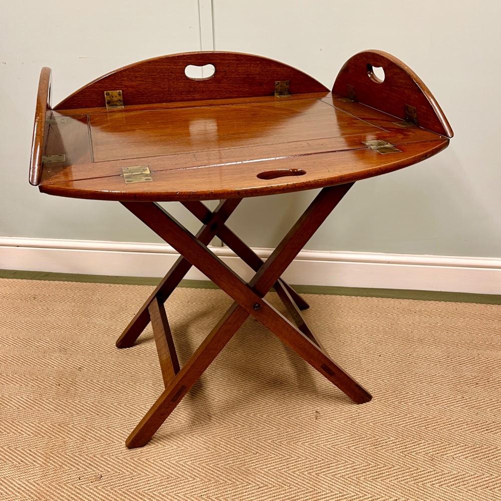 A 19th-century mahogany butlers tray featuring hinged drop sides and hand-cut handles set on a matching folding X-frame stand.