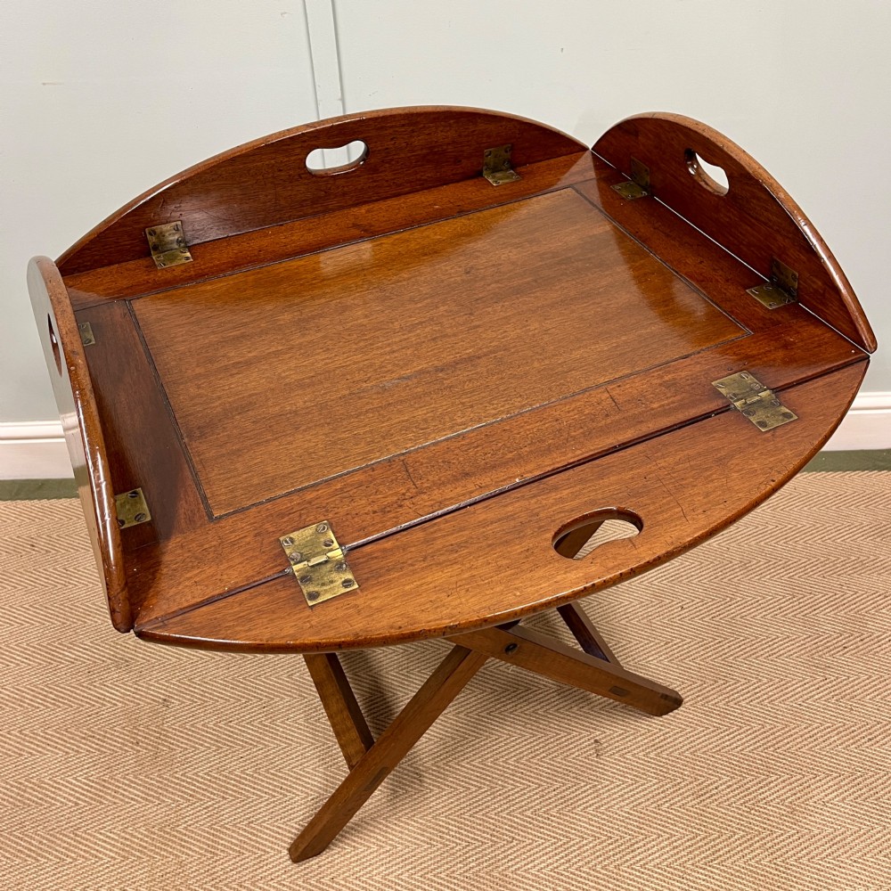 A 19th-century mahogany butlers tray featuring hinged drop sides and hand-cut handles set on a matching folding X-frame stand. View II