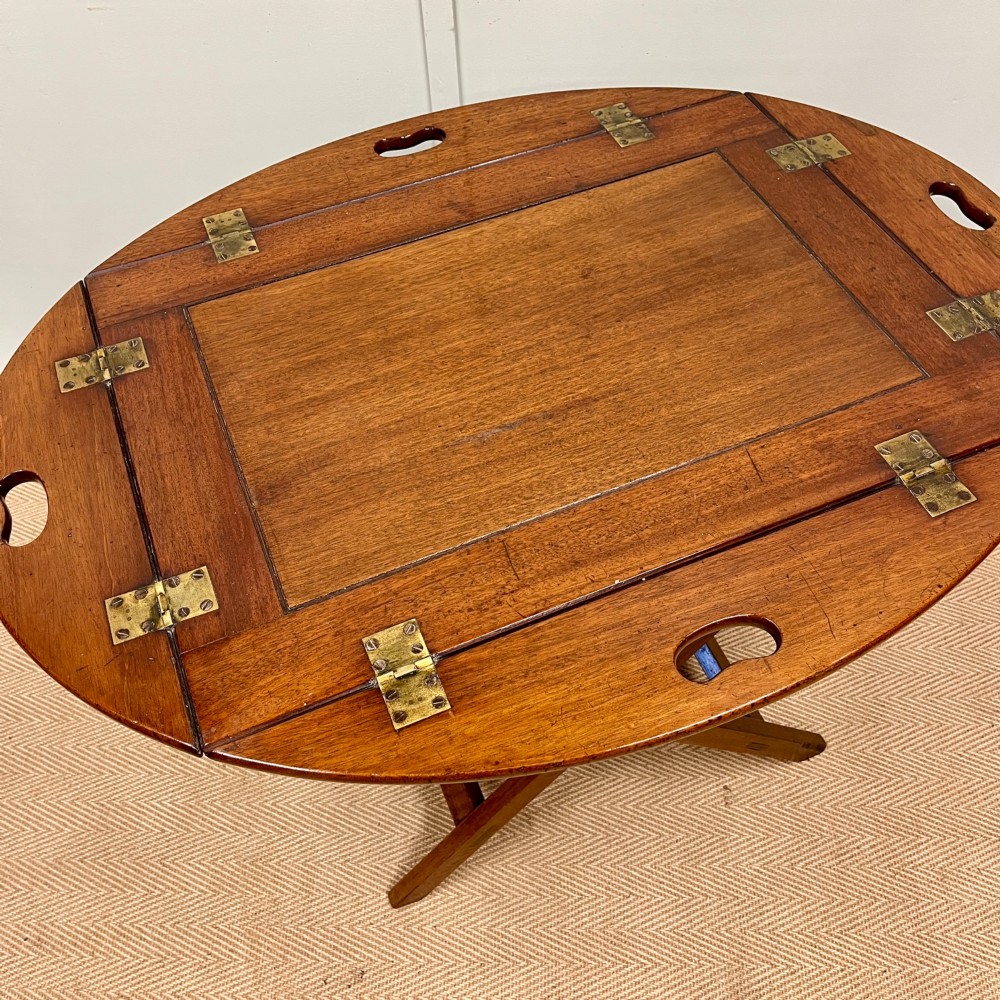 A 19th-century mahogany butlers tray featuring hinged drop sides and hand-cut handles set on a matching folding X-frame stand. View V