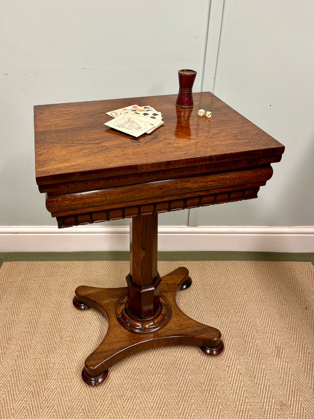 A 19th-century rosewood games table with a polished rectangular fold-over top, a faceted pedestal column, and a quadform base on flattened bun feet.