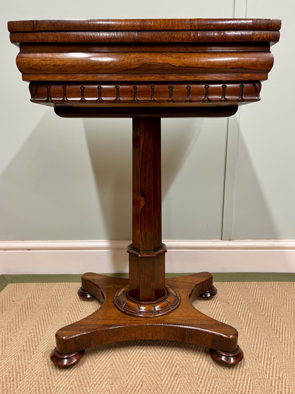 A 19th-century rosewood games table with a polished rectangular fold-over top, a faceted pedestal column, and a quadform base on flattened bun feet. View II