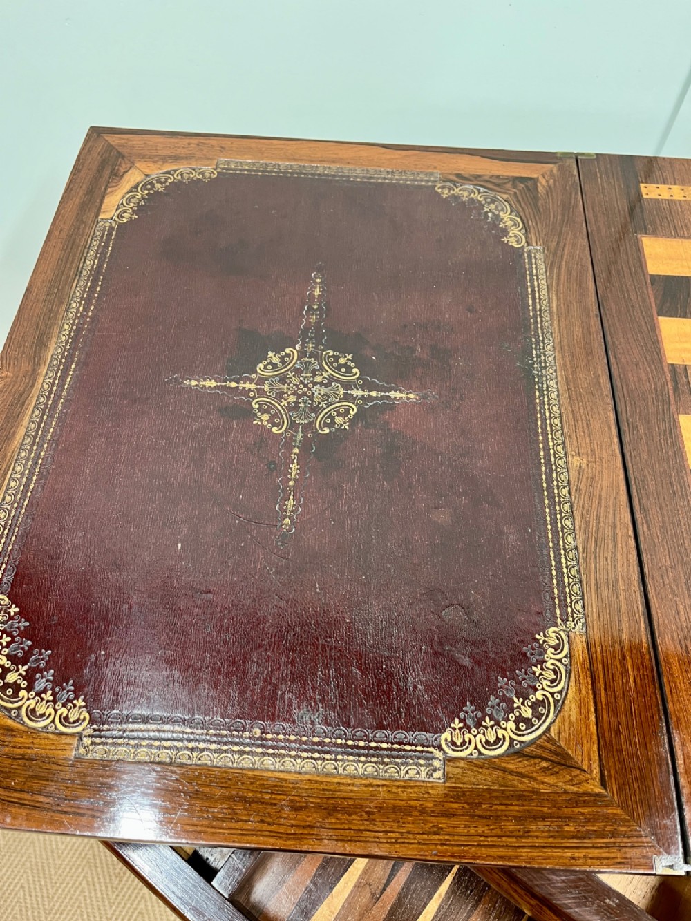 A 19th-century rosewood games table with a polished rectangular fold-over top, a faceted pedestal column, and a quadform base on flattened bun feet. View VI