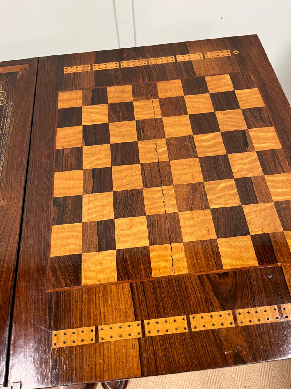 A 19th-century rosewood games table with a polished rectangular fold-over top, a faceted pedestal column, and a quadform base on flattened bun feet. View VII