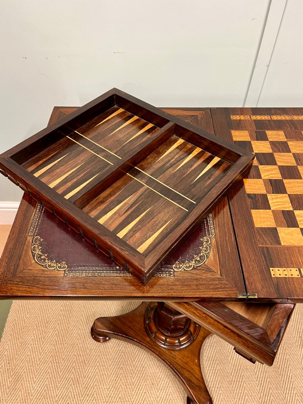 A 19th-century rosewood games table with a polished rectangular fold-over top, a faceted pedestal column, and a quadform base on flattened bun feet. View IX