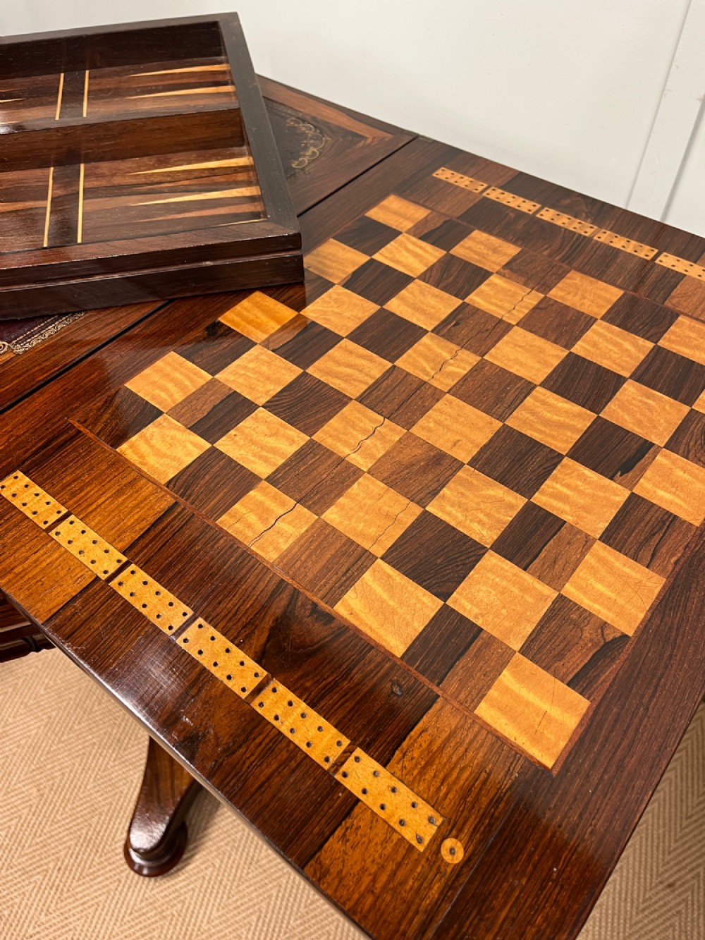 A 19th-century rosewood games table with a polished rectangular fold-over top, a faceted pedestal column, and a quadform base on flattened bun feet. View XI