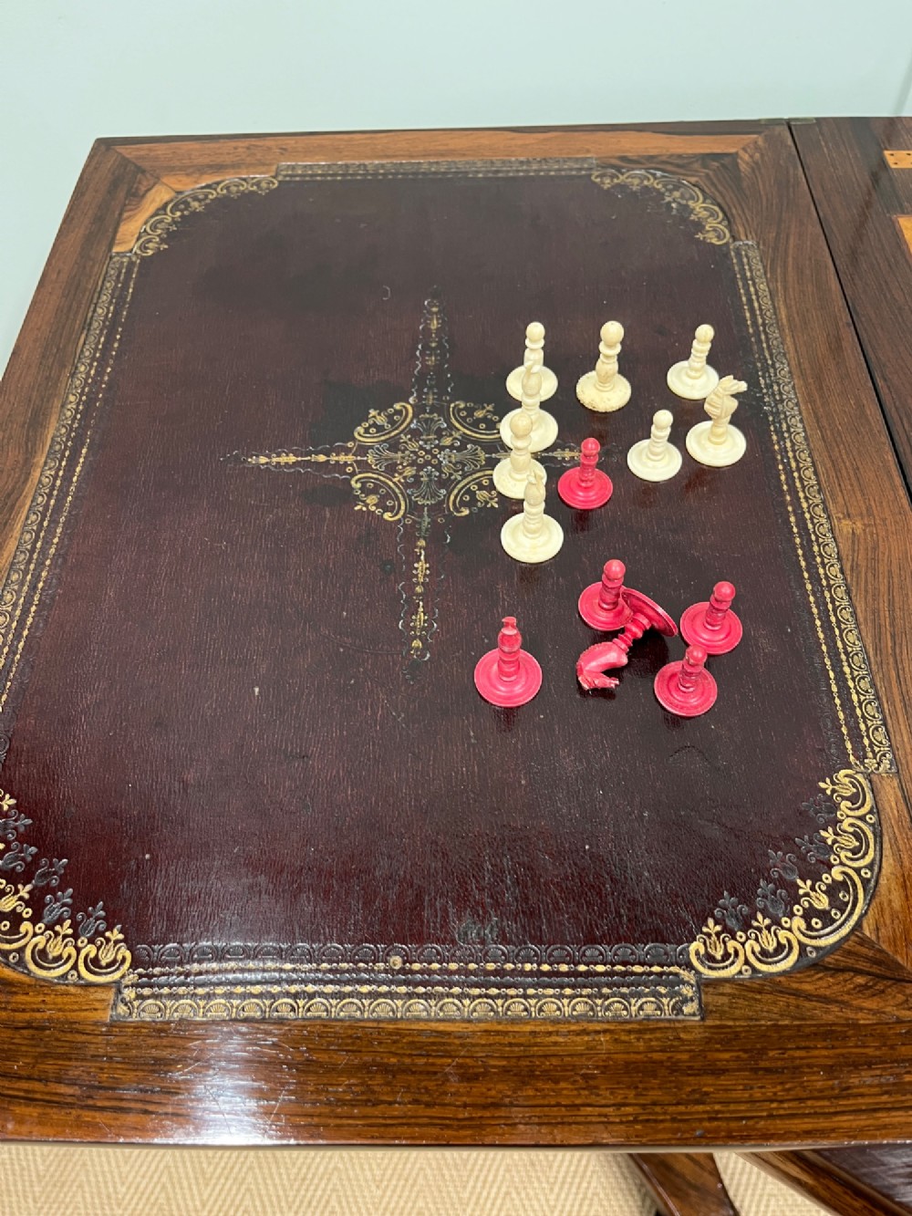A 19th-century rosewood games table with a polished rectangular fold-over top, a faceted pedestal column, and a quadform base on flattened bun feet. View XIV