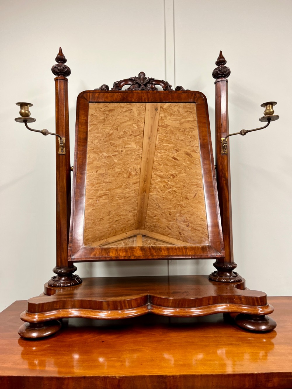 A 19th-century mahogany swing toilet mirror featuring carved support columns, two attached brass candle sconces, and a serpentine plinth base.