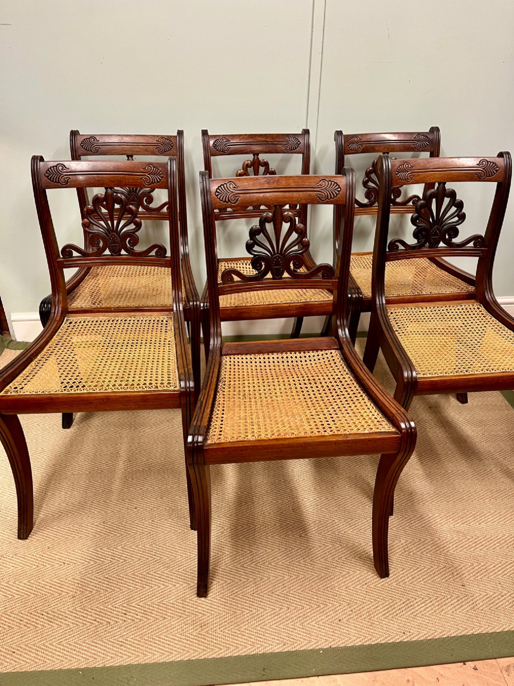 A set of six Regency carved rosewood dining chairs featuring carved anthemion back splats, sabre legs, and woven cane seats.