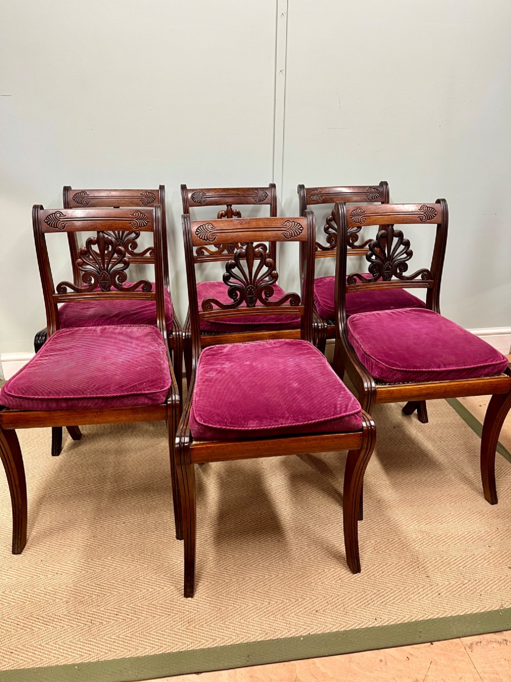 A set of six Regency carved rosewood dining chairs featuring carved anthemion back splats, sabre legs, and woven cane seats. View II