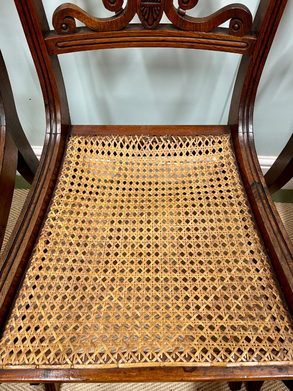 A set of six Regency carved rosewood dining chairs featuring carved anthemion back splats, sabre legs, and woven cane seats. View III
