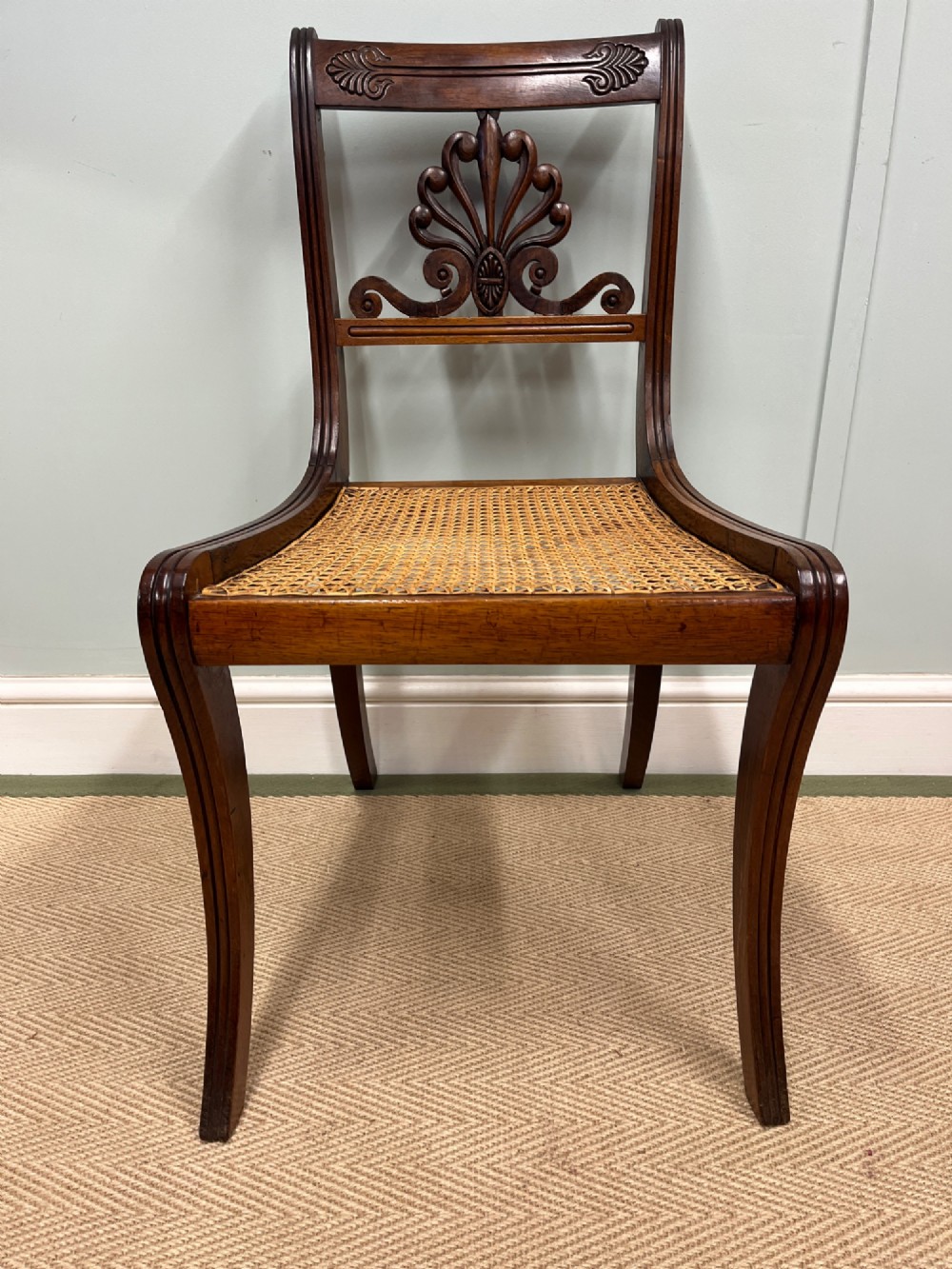A set of six Regency carved rosewood dining chairs featuring carved anthemion back splats, sabre legs, and woven cane seats. View VII