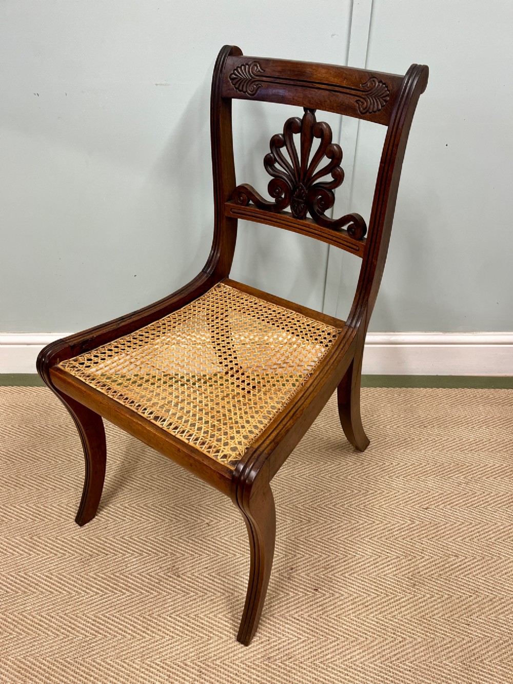 A set of six Regency carved rosewood dining chairs featuring carved anthemion back splats, sabre legs, and woven cane seats. View VIII
