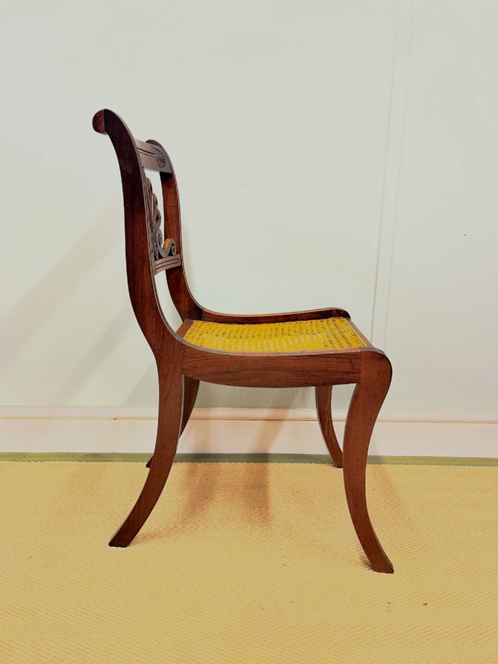 A set of six Regency carved rosewood dining chairs featuring carved anthemion back splats, sabre legs, and woven cane seats. View X
