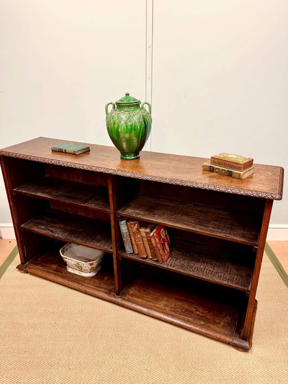 A low nineteenth-century open teak bookcase featuring two main sections with adjustable shelves and a carved egg-and-dart moulding along the top rim.