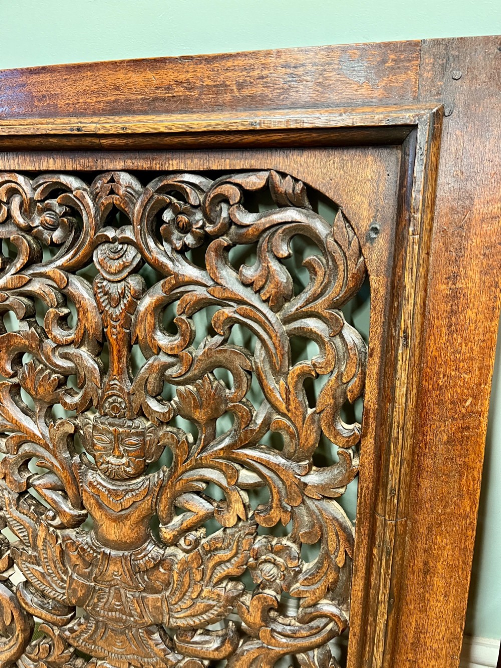 A pair of square dark teak wall panels featuring openwork floral and deity carvings surrounded by dark timber frames. View IV