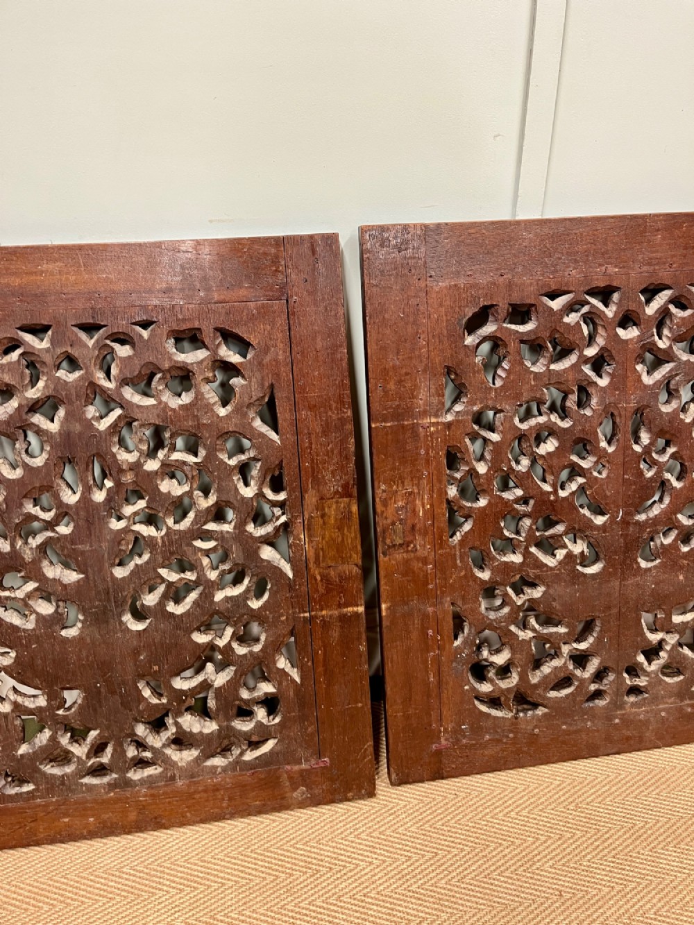 A pair of square dark teak wall panels featuring openwork floral and deity carvings surrounded by dark timber frames. View V