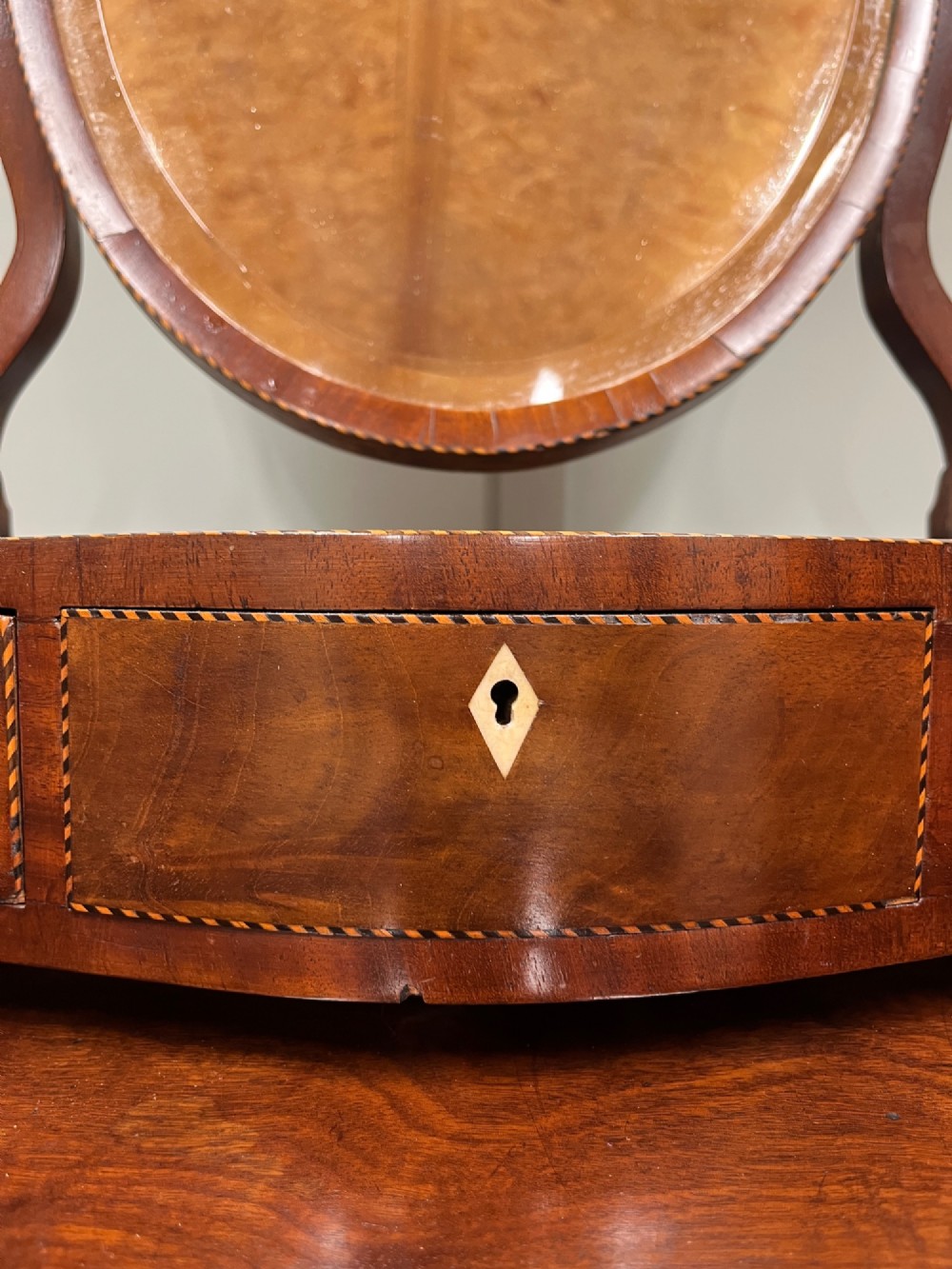 An antique Georgian mahogany toilet mirror featuring an oval adjustable glass frame mounted on curved supports above a three-drawer box base. View II