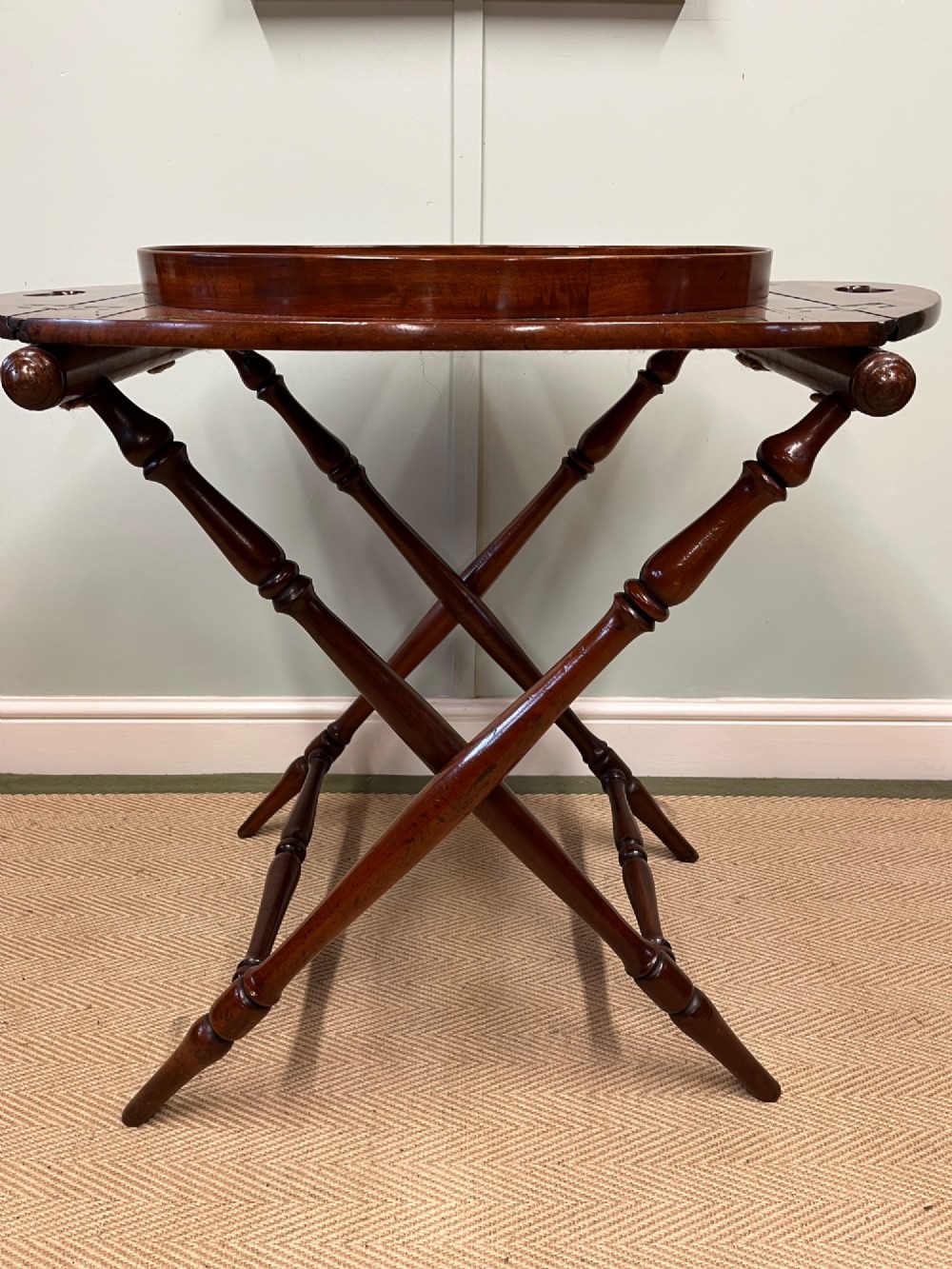 A 19th-century mahogany butlers tray with drop-down hinged sides and cutout hand-holes, set upon a turned folding X-frame stand. View II