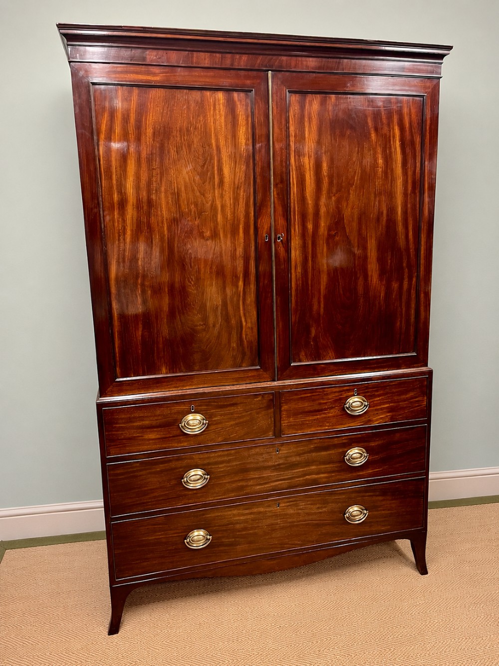 A Regency mahogany linen press featuring an upper two-door cupboard with flame veneer panels above a base of two short and two long drawers with brass handles.
