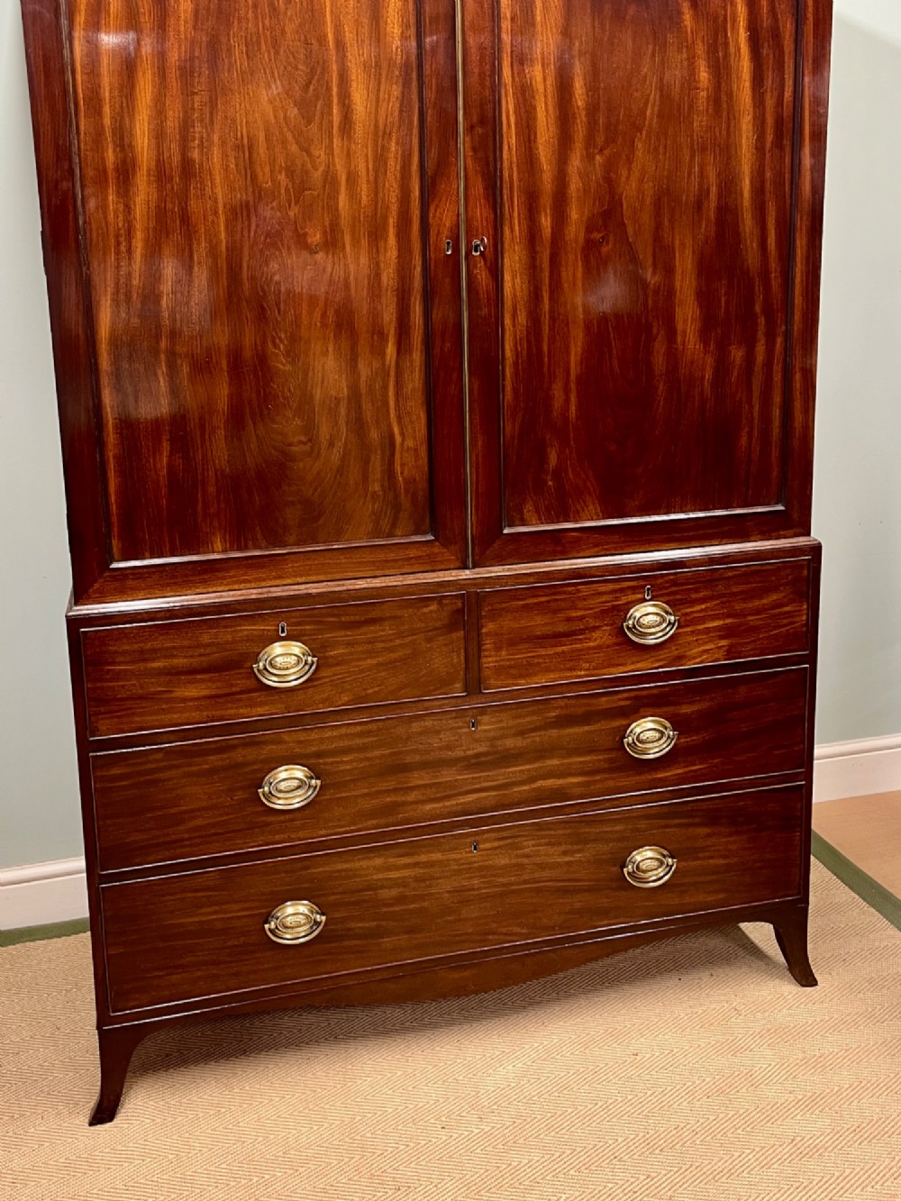 A Regency mahogany linen press featuring an upper two-door cupboard with flame veneer panels above a base of two short and two long drawers with brass handles. View II