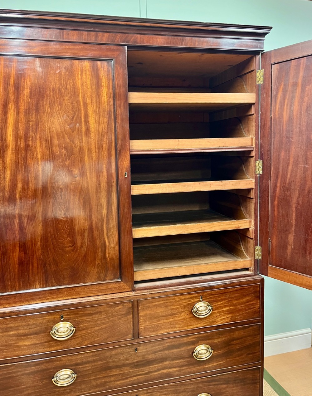 A Regency mahogany linen press featuring an upper two-door cupboard with flame veneer panels above a base of two short and two long drawers with brass handles. View III