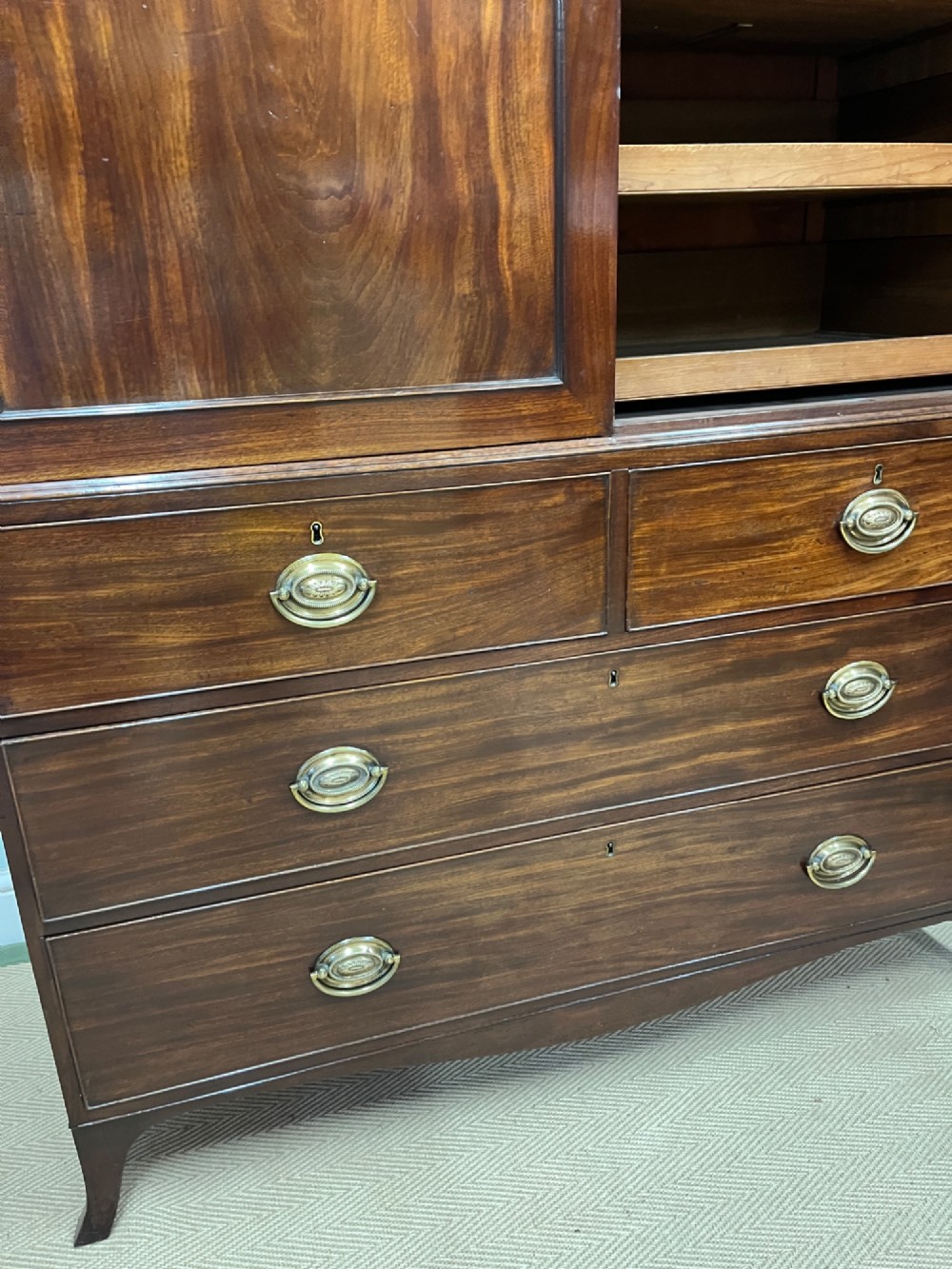 A Regency mahogany linen press featuring an upper two-door cupboard with flame veneer panels above a base of two short and two long drawers with brass handles. View V