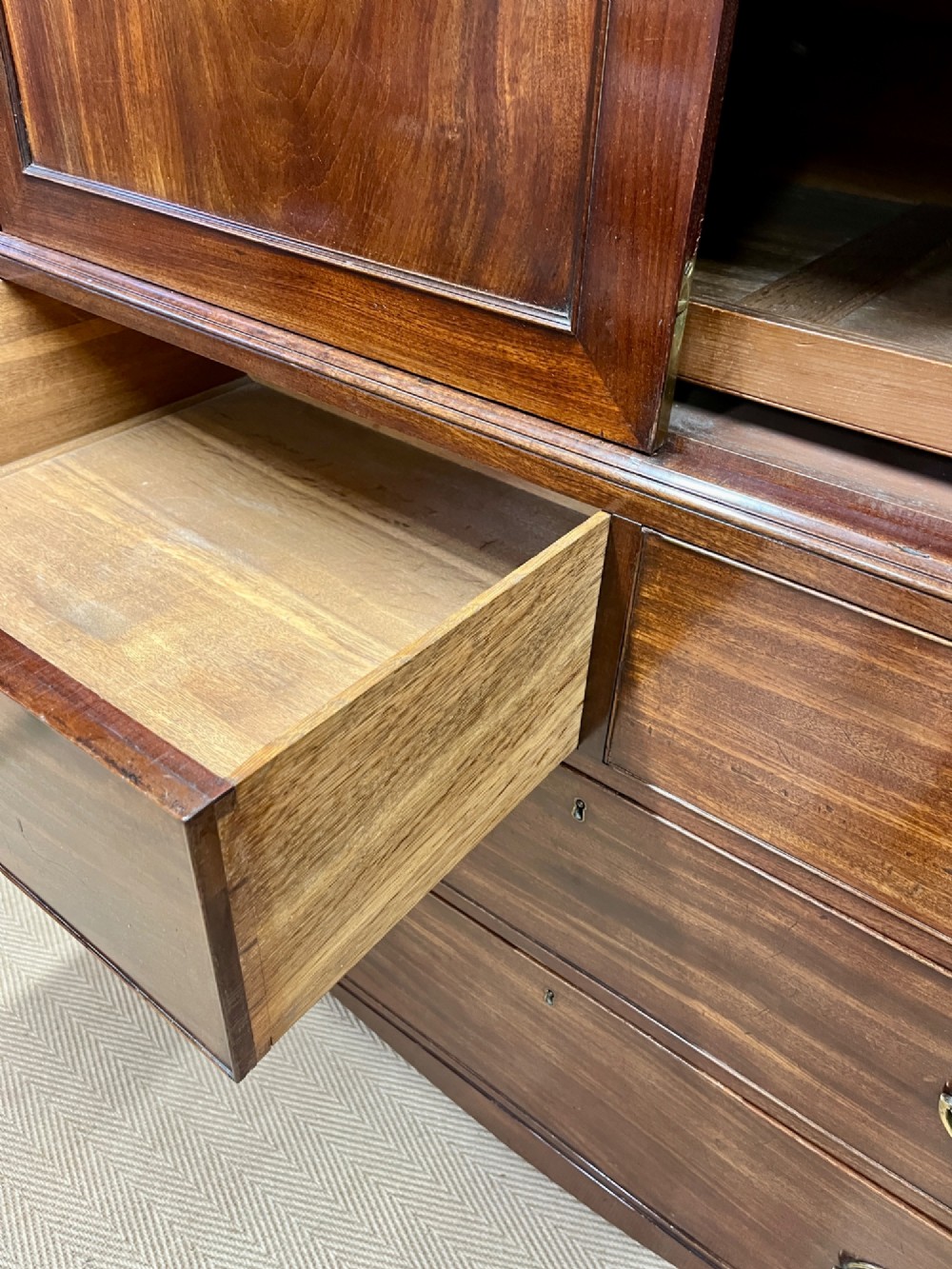 A Regency mahogany linen press featuring an upper two-door cupboard with flame veneer panels above a base of two short and two long drawers with brass handles. View VI