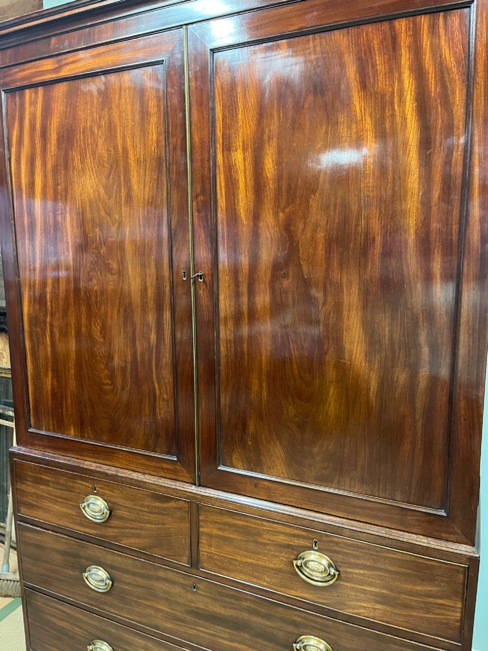 A Regency mahogany linen press featuring an upper two-door cupboard with flame veneer panels above a base of two short and two long drawers with brass handles. View IX