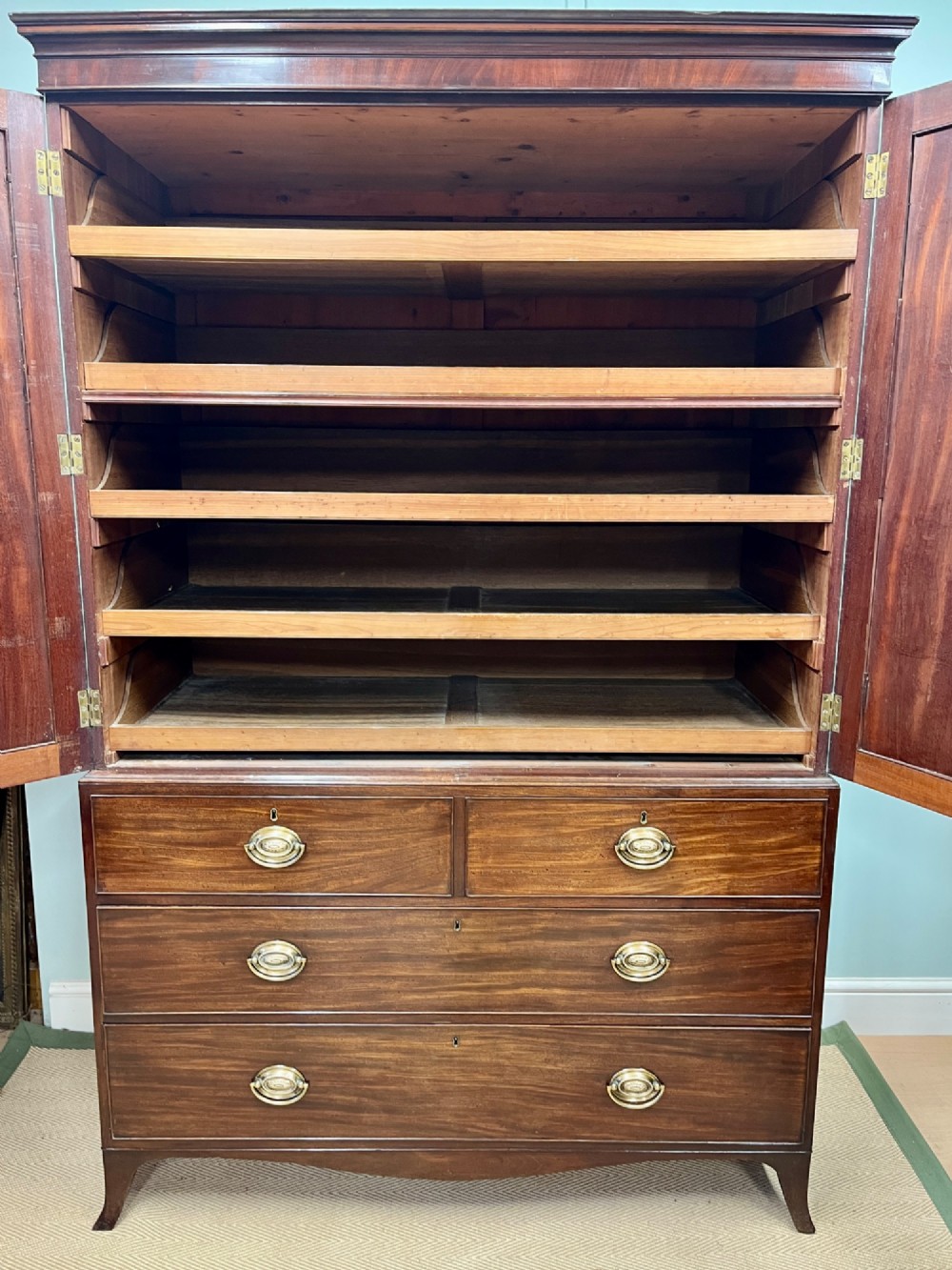 A Regency mahogany linen press featuring an upper two-door cupboard with flame veneer panels above a base of two short and two long drawers with brass handles. View X