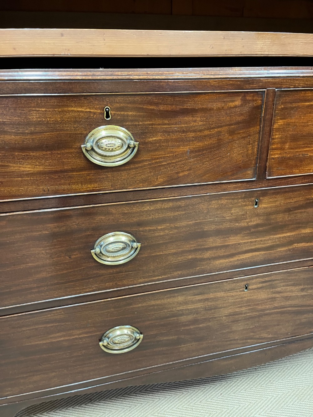 A Regency mahogany linen press featuring an upper two-door cupboard with flame veneer panels above a base of two short and two long drawers with brass handles. View XI