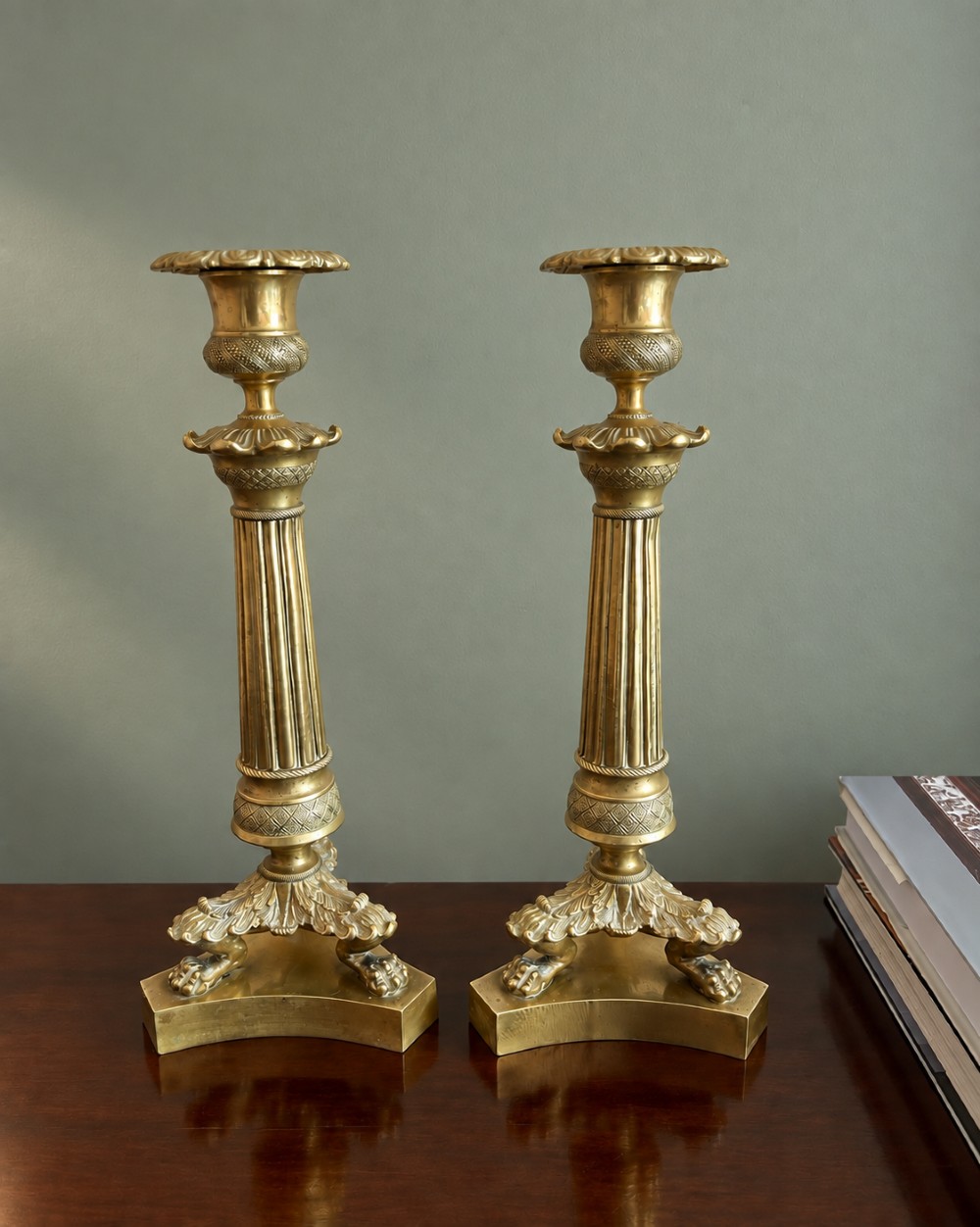 A pair of 19th-century Empire style cast brass candlesticks featuring fluted columns, engine-turned banding, and lion paw feet on tripartite bases. View II