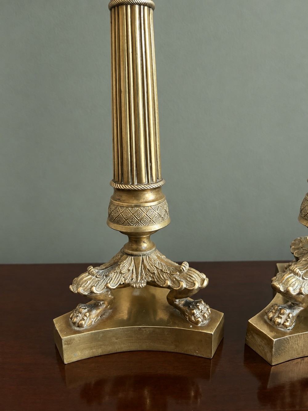 A pair of 19th-century Empire style cast brass candlesticks featuring fluted columns, engine-turned banding, and lion paw feet on tripartite bases. View III