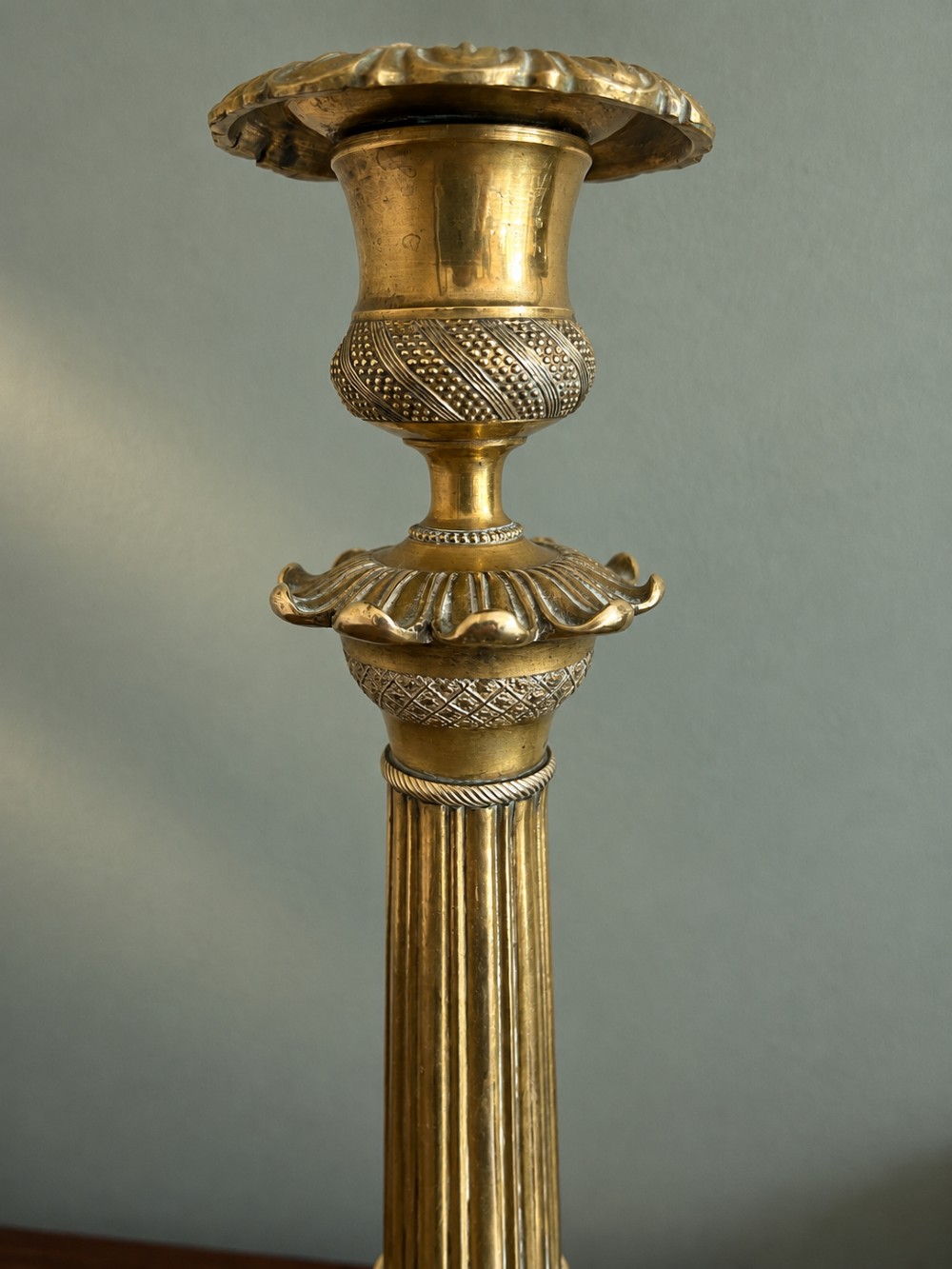 A pair of 19th-century Empire style cast brass candlesticks featuring fluted columns, engine-turned banding, and lion paw feet on tripartite bases. View V
