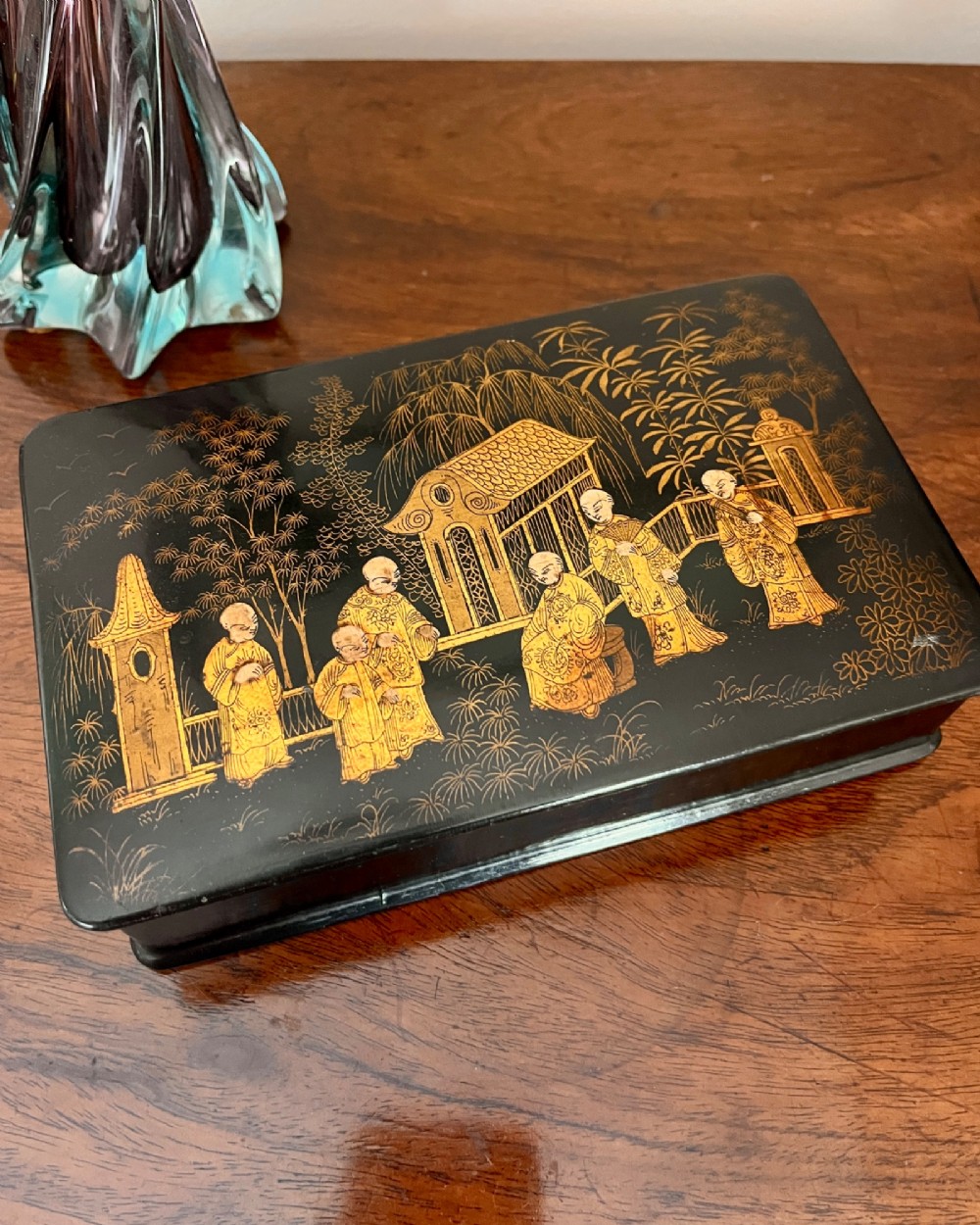 A rectangular black lacquered box decorated with detailed gold Chinoiserie scenes depicting figures, foliage, and pavilions. View II