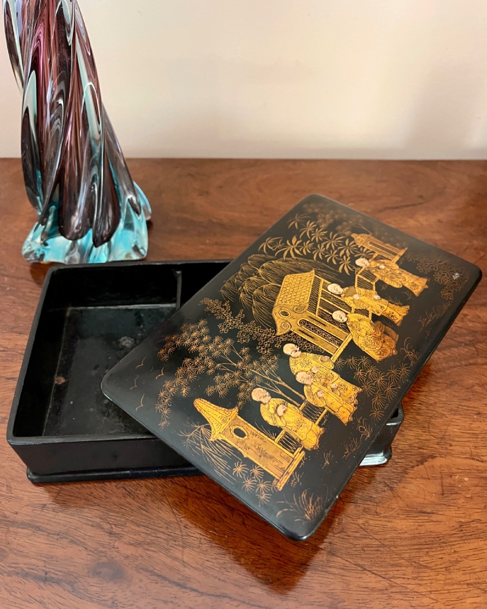 A rectangular black lacquered box decorated with detailed gold Chinoiserie scenes depicting figures, foliage, and pavilions. View III
