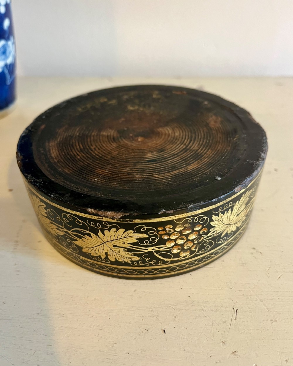 A circular black lacquered Regency papier-mache wine coaster decorated with gilded grape vine motifs around the exterior rim. View II