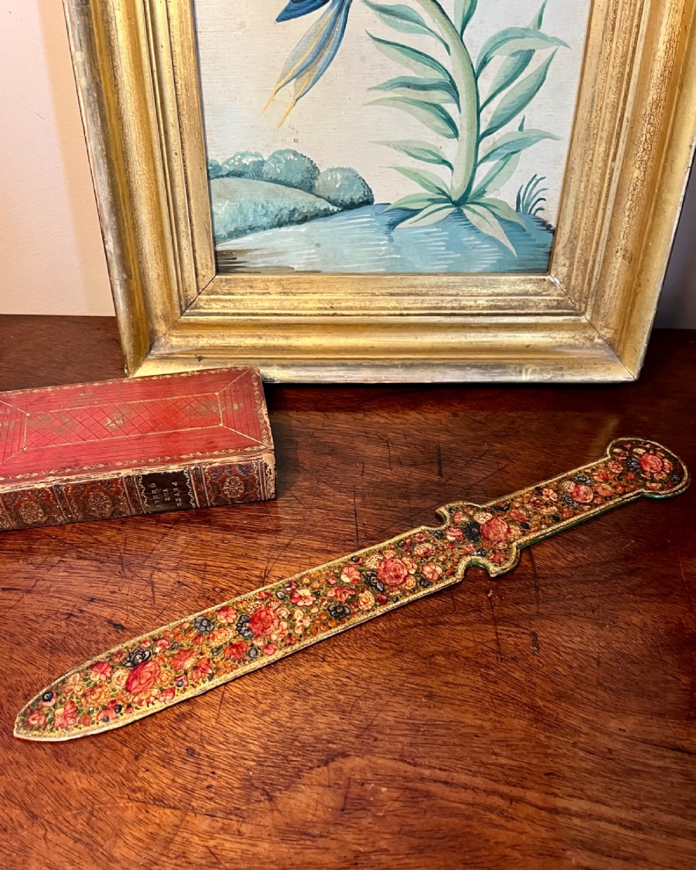 A 19th-century Kashmiri papier-mache letter opener featuring dense hand-painted polychrome floral decoration and gold detailing over a dark lacquered surface.