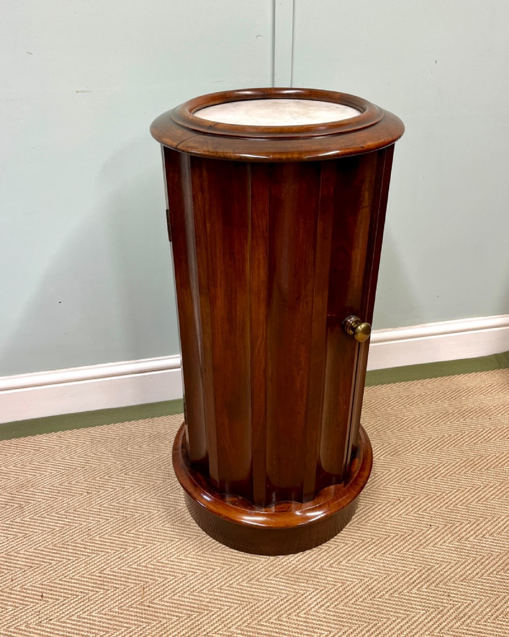 A 19th-century cylindrical dark mahogany pot cupboard featuring vertical fluting, a circular inset marble top, a single curved door, and a brass knob.