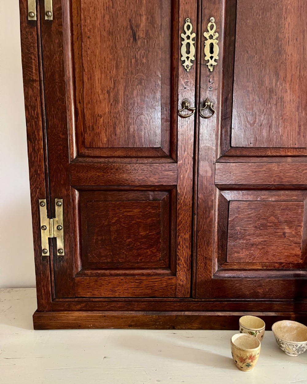 An eighteenth-century dark oak wall cupboard featuring twin arched fielded panel doors and prominent brass H-hinges. View II