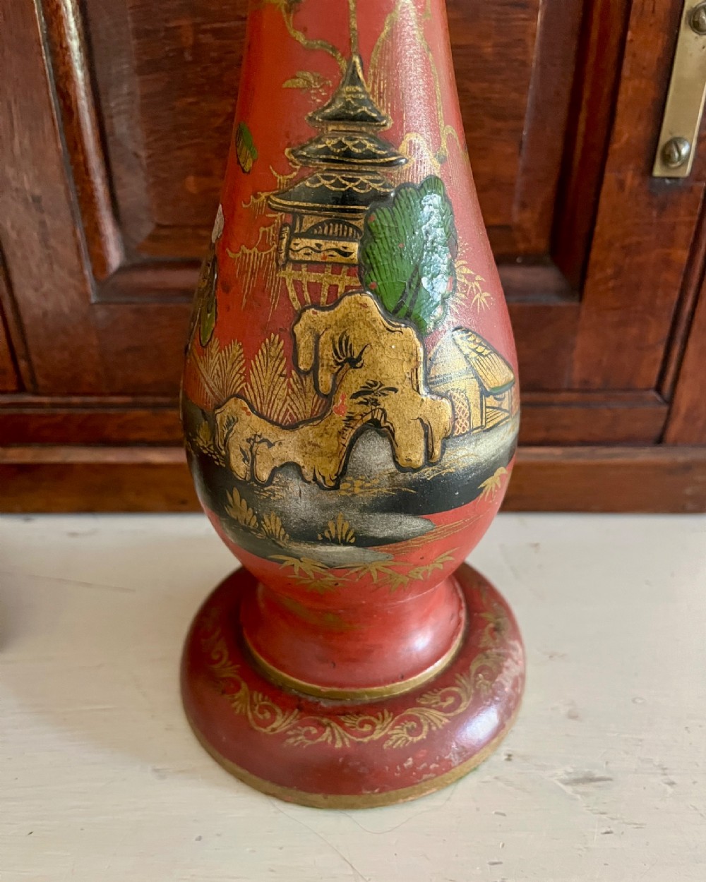 A red lacquered table lamp featuring hand-painted gilt Chinoiserie figures and pagodas on a circular base with a brass bulb socket. View II