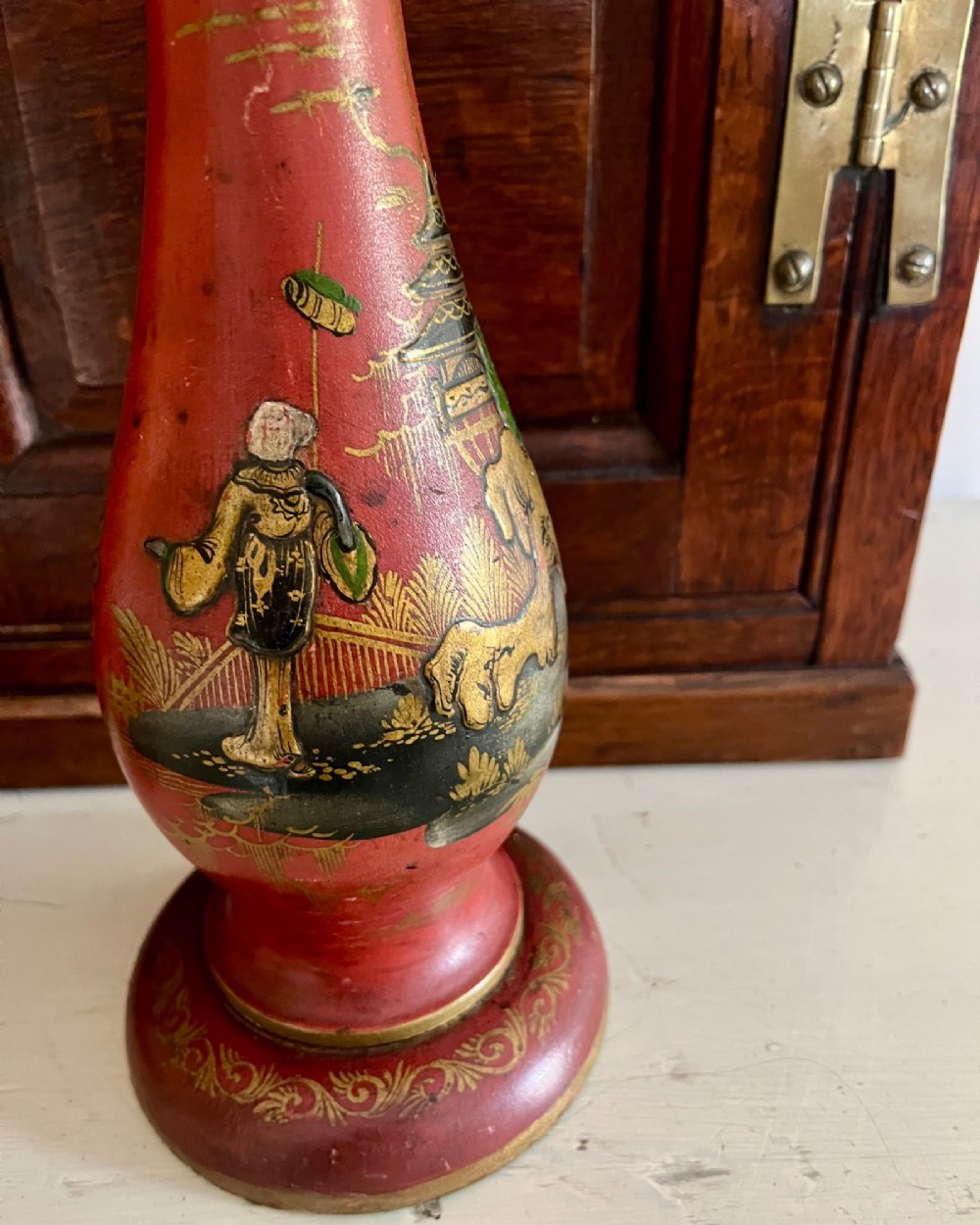 A red lacquered table lamp featuring hand-painted gilt Chinoiserie figures and pagodas on a circular base with a brass bulb socket. View III