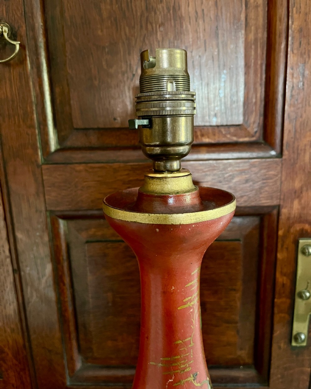 A red lacquered table lamp featuring hand-painted gilt Chinoiserie figures and pagodas on a circular base with a brass bulb socket. View IV