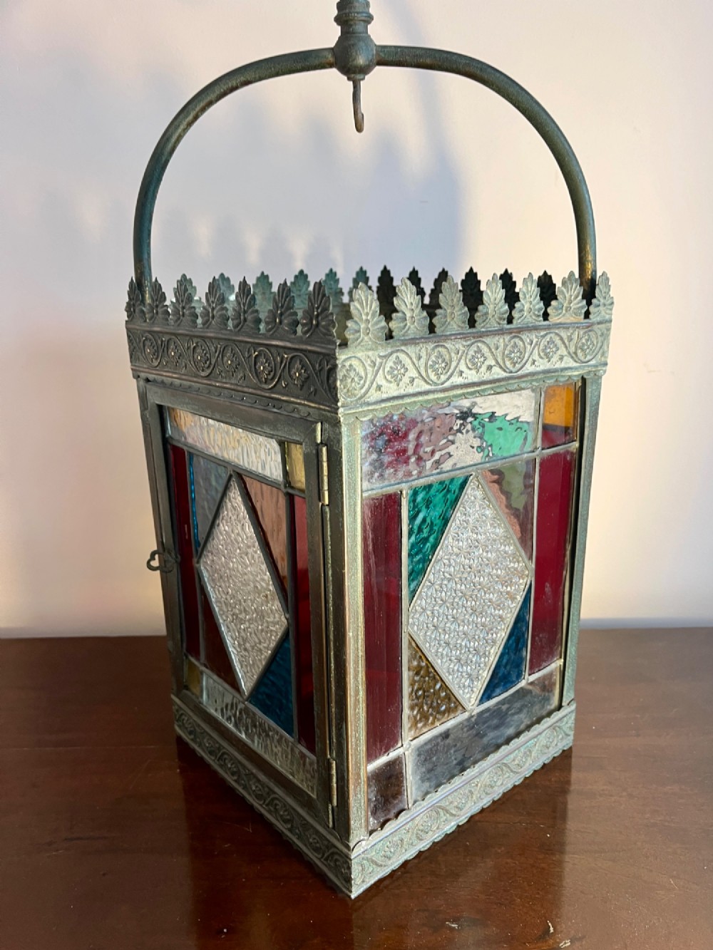 A nineteenth-century four-sided brass hall lantern featuring multi-coloured stained glass panels and a decorative cresting rim suspended from an arched handle. View II