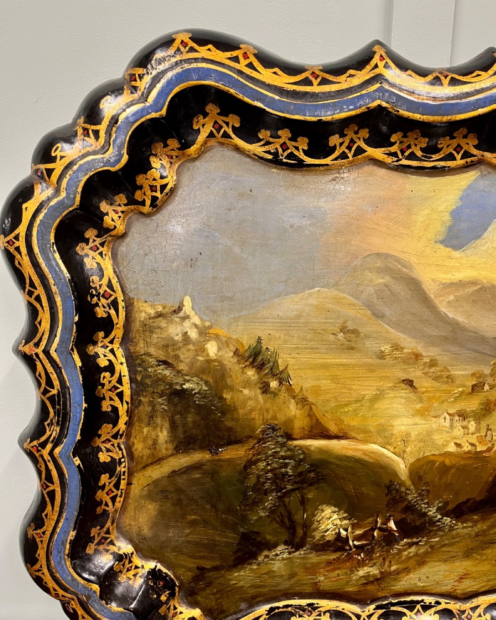 A black scalloped Regency papier-mache tray featuring a hand-painted mountain landscape encircled by a gilded decorative border. View II