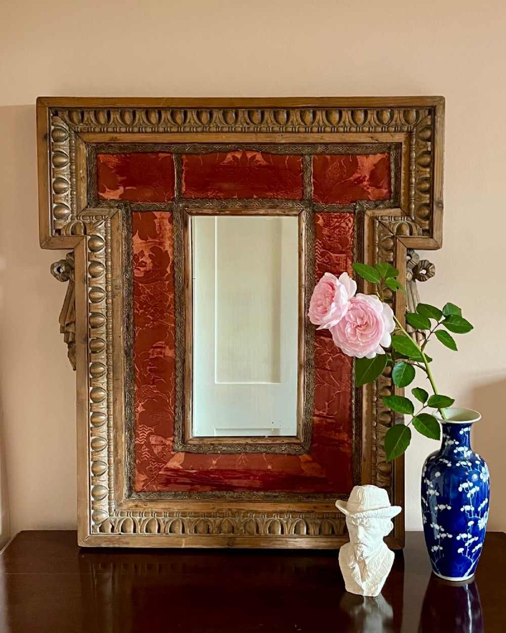 An 18th-century carved pine wall mirror featuring egg-and-dart outer borders, side ear brackets, and a red damask fabric panel surrounding the central rectangular glass plate.