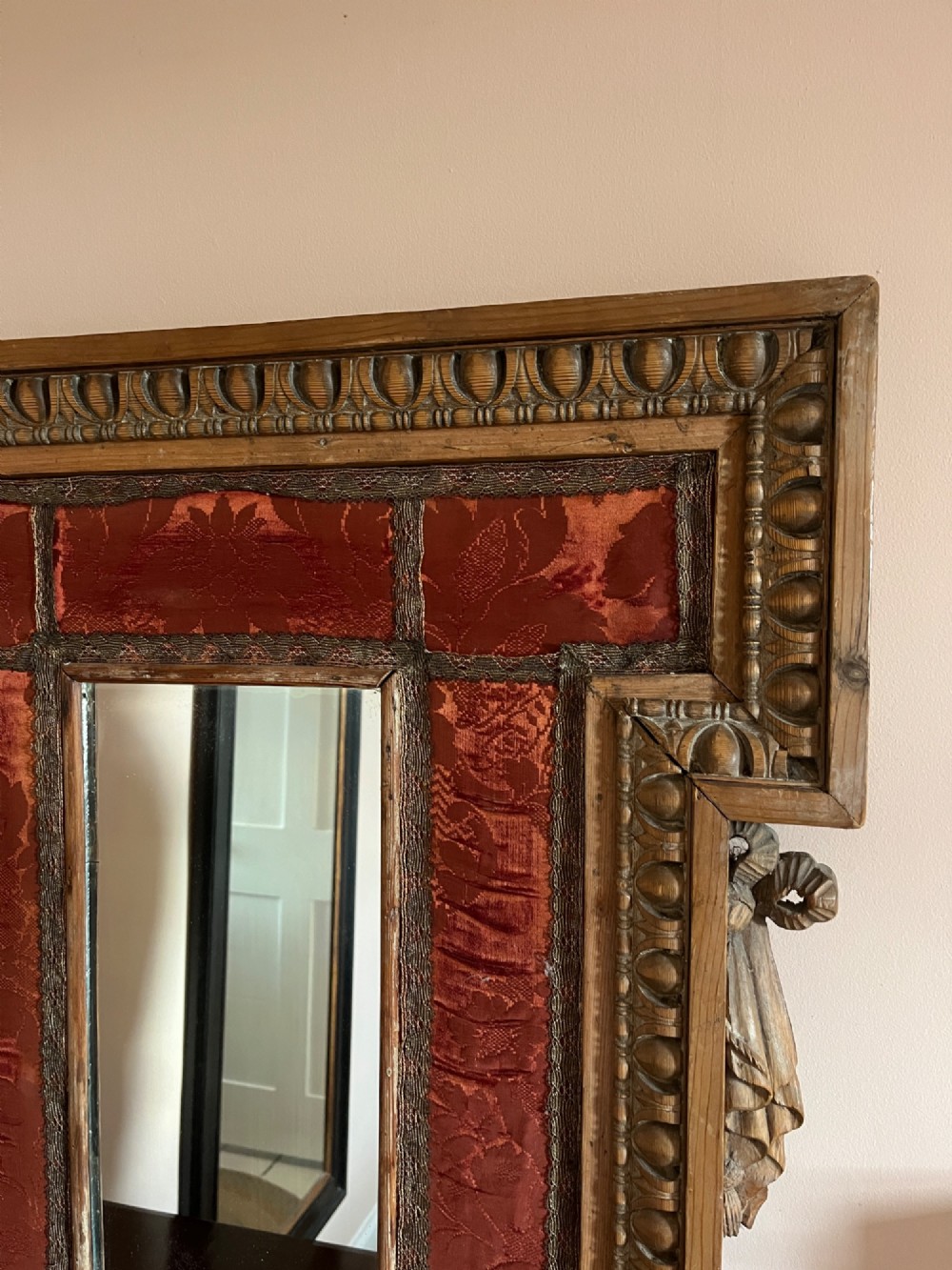 An 18th-century carved pine wall mirror featuring egg-and-dart outer borders, side ear brackets, and a red damask fabric panel surrounding the central rectangular glass plate. View II